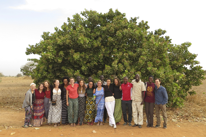 A group of students and Senegalese pose in front of a tree